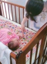 ベビーベッドの赤ちゃんを見守る子ども